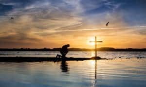 Man kneeling near cross off shore