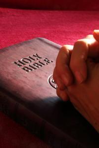 folded hands on a Holy Bible