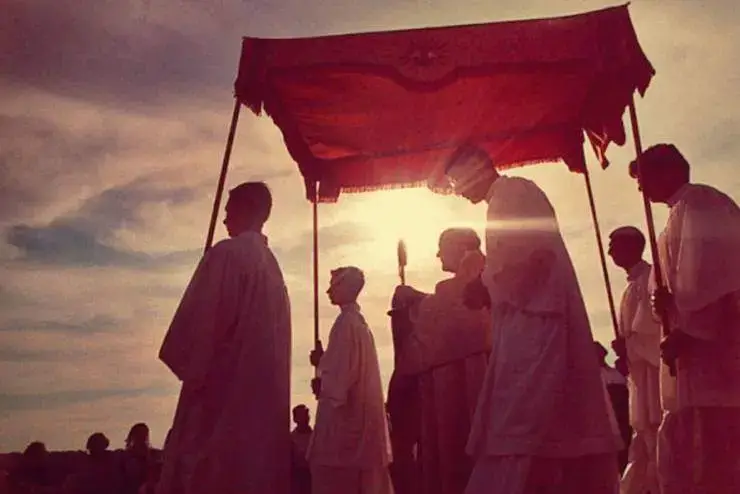 Catholics walk beneath a canopy during a Eucharistic procession at sunset